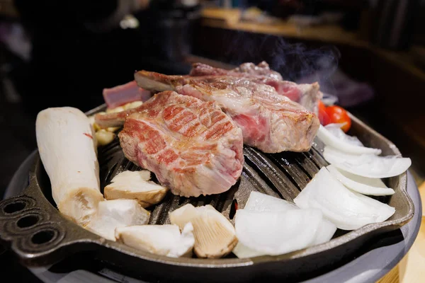 Sizzling Korean barbecue beef on grill with steam rising, showcasing traditional Asian cuisine and street-style restaurant food.
