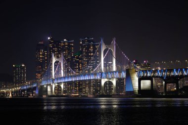 BUSAN, Güney Kore, 18 Aralık 2025. Gwangan Köprüsü 'nün gece görüşü. Şehir ışıkları denize yansıyor. İkonik Busan simgesi ve seyahat, turizm ve reklamcılık için kentsel gece geçmişi.