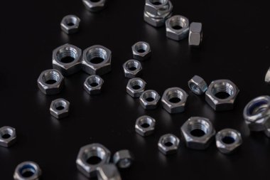 Siyah zemin üzerinde metal fındıklar, mekanik montaj için endüstriyel donanım bileşenleri, bağlanma ve mühendislik kullanımı, inşaat malzemeleri konsepti ve hassasiyet imalatı