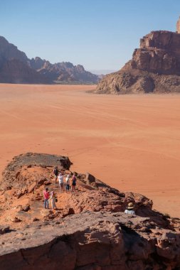 İnsanlar engin çöl manzarasında kayalık araziyi keşfediyorlar.