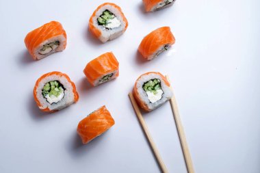 Beyaz arka planda yemek çubuklarıyla sıralanmış suşi dilimleri.