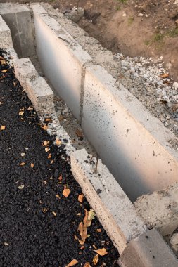 Çakıl ve yapraklarla çevrili beton drenaj çukuru.