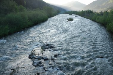 Yeşil ağaçlar ve dağlarla çevrili akan nehir.