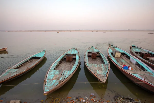Sakin bir nehre demirlemiş, sisli gökyüzünün altında mavi boyalı birkaç geleneksel ahşap tekne.