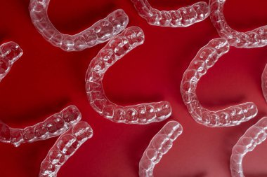 Görünmez ortodonti esansı, bu net hizalayıcılar tarafından güzel bir şekilde iletilir. Cesur, kırmızı bir arkaplanda düzenlenmiştir..