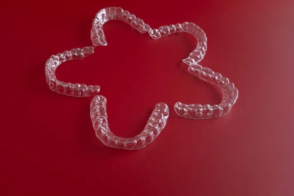 Modern diş düzeltme araçları yenilikçi diş hizalamalarını gösteren dinamik kırmızı bir tuval üzerinde sunulmaktadır..