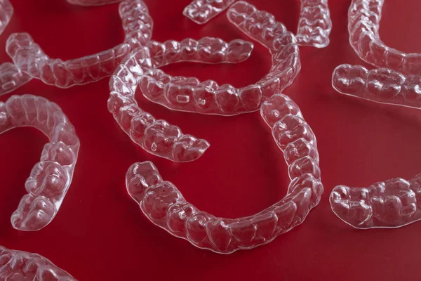 Görünmez diş dizginleri, modern dişlerin düzgün durmasını sağlayan, koyu kırmızı bir yüzeyde sanatsal olarak düzenlenmiştir..