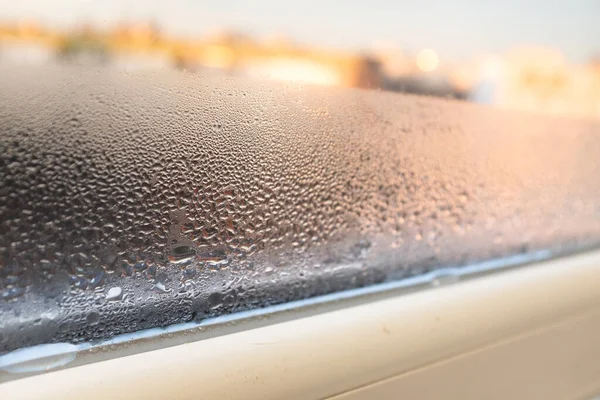 Gökyüzü ve güneş ışığının yumuşak ve parlak arkaplanına karşı yoğun yoğunlaşmayla kaplı pencere camı, yalıtım sorunlarını, nemi veya iklim kontrolünü sembolize eder.