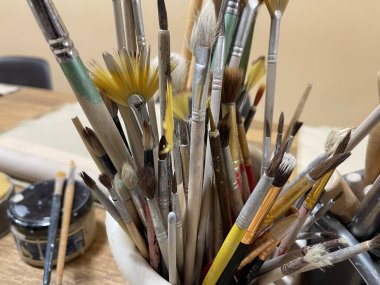 Ahşap ve metal saplı çeşitli sanat fırçalarının yoğun koleksiyonu dağınık, yaratıcı bir sanat stüdyosunda beyaz bir kapta saklanıyor.