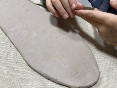 Çocuğun nazikçe bej renkli modelleme kil tabakasına bastırması, yaratıcılığı, çocukluk sanatını, duyusal oyunu, çömlek ya da seramik stüdyosu kavramlarını vurgulaması.