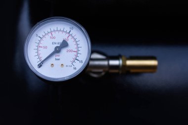 Sıkıştırılmış hava veya gaz için basınç göstergesi (manometre) yakın plan, PSI ve Çubukta çift ölçekli görüntüleme, koyu, bulanık arkaplana karşı metalik bir bağlantı parçasına monte edilir.