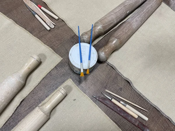 Kil levha yuvarlama ve heykel düzeneği, merdaneler, ahşap çıtalar, oyma araçları, ve çömlek ve seramik el işi için desenli bir çuval bezi yüzeyi üzerinde ham kil topaklar