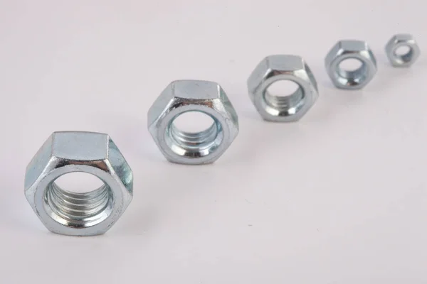 Beyaz zemin üzerinde metal fındıklar, mekanik montaj için endüstriyel donanım bileşenleri, bağlanma ve mühendislik kullanımı, inşaat malzemeleri konsepti ve hassasiyet üretimi