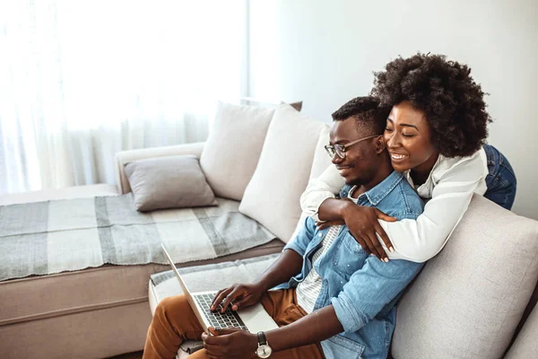 Cheerful happy African American young marriage laughing while watching movie on laptop computer at home interior, happy dark skinned couple in love shopping online on netbook enjoying store discounts