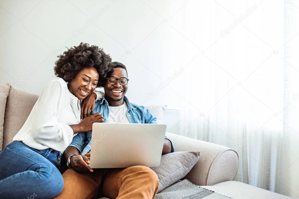 Cropped shot of a couple using a laptop while sitting on the sofa. Smiling couple watching movie on laptop. Man and woman are relaxing on couch. They are spending leisure time at home.