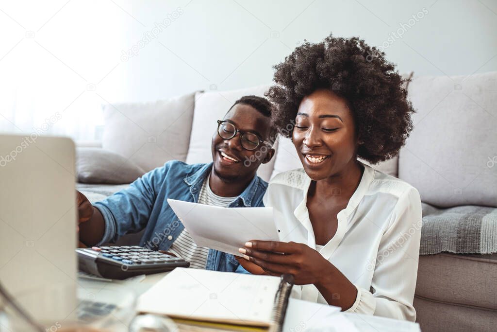 Photo of cheerful loving young couple using laptop and analyzing their finances with documents. Look at papers. Happy couple at home paying bills with lapto