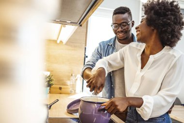 Çekici çift mutfakta yemek pişiriyor. Birbirinize bakıp gülümsüyorsunuz. Mutlu çift evlerinin mutfağında birlikte yemek pişiriyor. Siyah çift mutfakta yemek pişiriyor.. 
