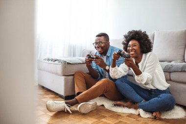 Evde video oyunu oynayan genç bir çiftin fotoğrafı. Onlar dost canlısı rakiplerdir. Randevu gecesinde video oyunu oynayan sevimli genç çift. Konsolda oyun oynayan güzel çift
