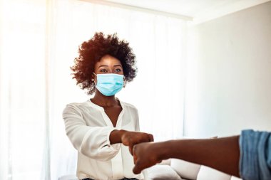 Hijyenik yüz maskesi takan genç kadınlar yumruk tokuşturarak selamlaşıyorlar. Koronavirüsten (Covid-19) korunan gençler.