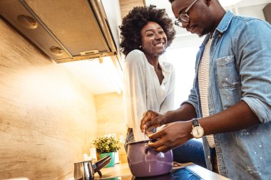 Yemek pişirme hobisi yaşam tarzı konsepti. Afro-Amerikalı mutlu çift sağlıklı yemekler pişiriyor ve evlerindeki çatı katındaki mutfaklarında birlikte eğleniyorlar.. 