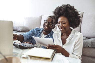 Aile sigortası konsepti. Olumlu siyahi çift evde belge okuyor, anlaşma detaylarını birlikte kontrol ediyorlar. Koltukta oturan genç Afrikalı çift Fatura Hesaplıyor