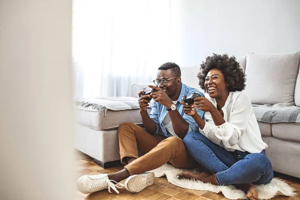 Did it! The best team ever. Beautiful lovers on a date indoors, they are playing video games. Their team have won, they are giving high five to celebrate. Smiling young couple playing video game by joysticks on floor at home