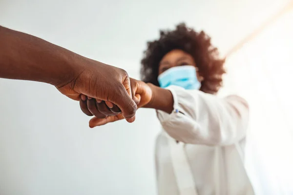 Colleagues giving each other a fist bump in a modern office,alternative greeting for safety and protection during COVID-19. Fist bump greeting between male and female adult with protective face mask.