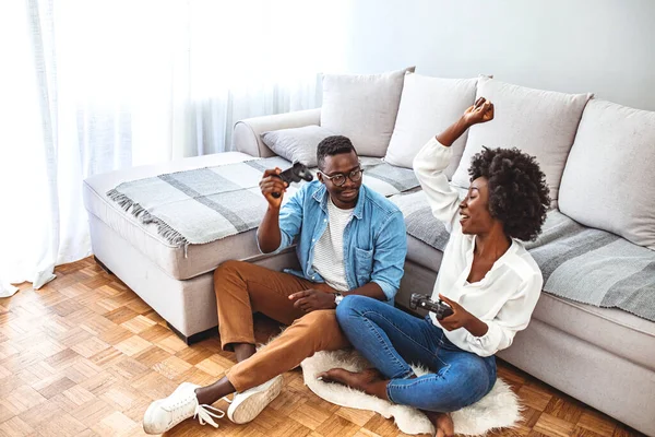 这对快乐的夫妇在客厅的沙发上玩电子游戏 这对笑容可亲的夫妇躺在地板上玩游戏 穿睡衣的年轻夫妇一起玩电子游戏 — 图库照片