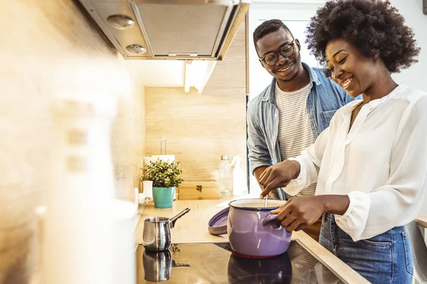 Cute joyful couple cooking together and adding spice to meal, laughing and spending time together in the kitchen. Cooked with love. Cropped shot of a young married couple tasting the food they are making in the kitchen at home