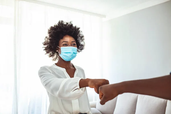 Young women wearing a hygienic face mask greeting by bumping fists together. Teenage realizing the self-protection against coronavirus (Covid-19) infection.