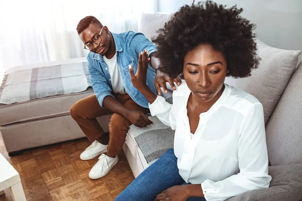 Unhappy young millennial married couple sitting on couch in living room after quarrel fight. Angry husband frustrated offended wife at home. Break up, divorce and misunderstanding in relations concept