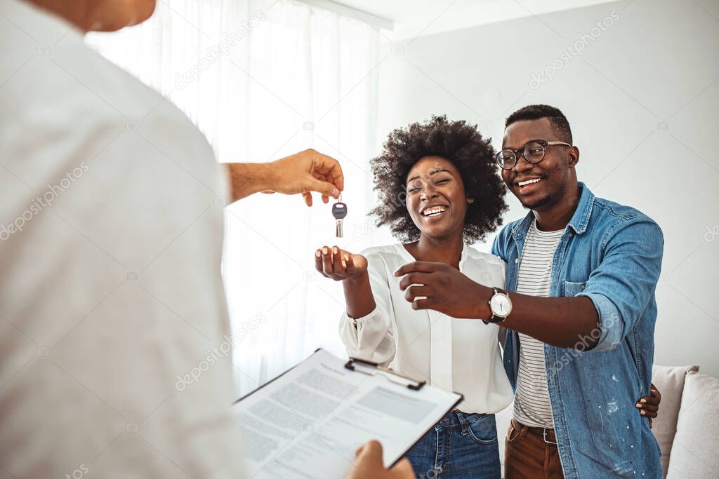 Photo of a smiling young couple thanking to the agent for the new house. Homeowners receiving their new house keys. Close up of a happy homeowners receiving their new house keys from a real estate agent at office