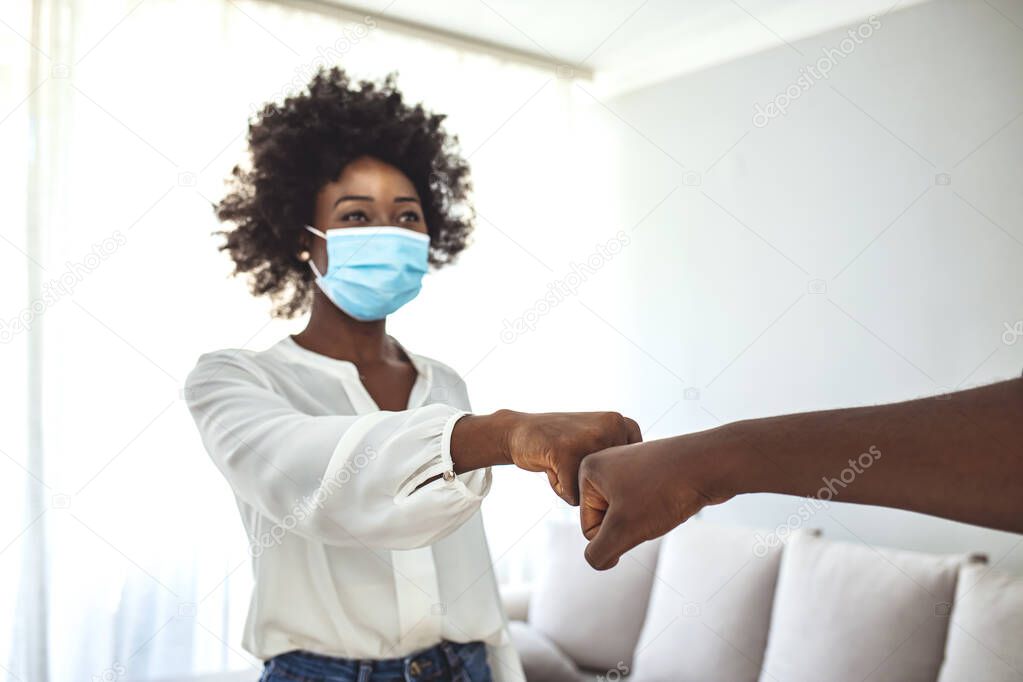 Young couple with protective face mask gesturing alternative greeting and handshakes,fist bump indoors, new normal concept in pandemic conditions. Two  friends wearing medical mask. Bump fists standing .