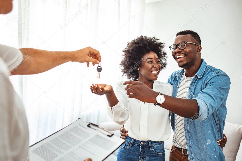 Handsome realtor is giving key to the new apartment to happy young couple. Couple buying new apartment.  A young couple receive the keys to their new apartment from a letting agent.