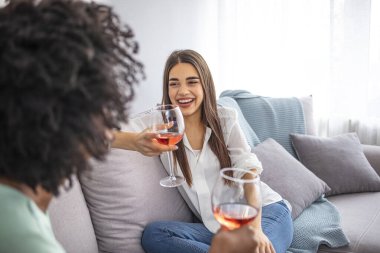 Kanepede oturan kadınlar sıcak bir dairede şarapla gülüyorlar. İki bayan arkadaş evde kanepede oturup bir bardak şarapla sohbet ediyorlar.. 