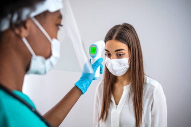 Açık hava salgını sırasında kontrol noktasında yüz maskeli bir genç kadının kızılötesi termometresiyle ısıyı ölçmek. Virüsün yayılmasını önleme kavramı