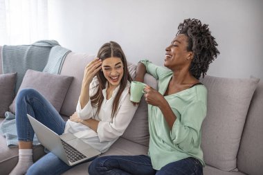 İki güzel genç bayan oturma odasında dinleniyor dizüstü bilgisayara bakıyor ve ekrandaki bir şeye gülüyor. Kadın arkadaşlar evde eğleniyor, dizüstü bilgisayar kullanıyorlar.