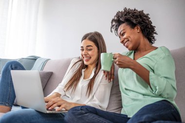 İki bayan arkadaş evde birlikte vakit geçiriyorlar, dizüstü bilgisayar ve dijital tablet kullanıyorlar, kanepede oturuyorlar. kopyalama alanı. Neşeli kadınlar web sörfü, oturma odası iç mekan