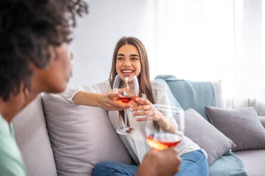 Kanepede oturan kadınlar sıcak bir dairede şarapla gülüyorlar. İki bayan arkadaş evde kanepede oturup bir bardak şarapla sohbet ediyorlar.. 