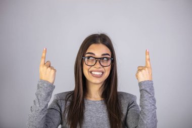 İşaret parmaklarıyla yukarıyı gösteren kadınlar, gri arka planda izole edilmiş gündelik giysiler içinde hoş bir şekilde gülümsüyor. Bu taraftan..
