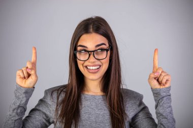 İşaret parmaklarıyla yukarıyı gösteren kadınlar, gri arka planda izole edilmiş gündelik giysiler içinde hoş bir şekilde gülümsüyor. Bu taraftan..