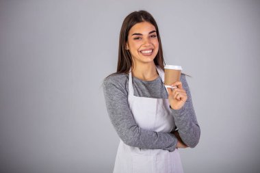 Kahveyle gülümseyen güzel bir garson. Gri arka planda izole edilmiş bir fincan sıcak kahveyi tutan ve servis eden bir garson. Bayan garson kafeterya sahibi. El ele tutuşun. Kağıt bardaklar. Sıcak içecek.