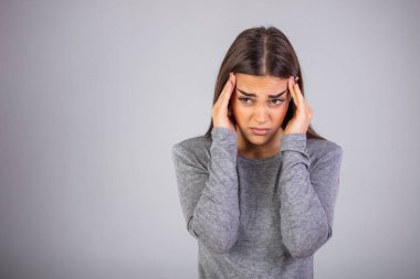 Başım ağrıyor. Umman el ele tutuşuyor ve gri arka planda dikilirken gözlerini kapalı tutuyor. Baş ağrısı çeken, strees hisseden bir kadın. Stüdyo fotoğrafı, günlük kıyafetler, gri arka plan..
