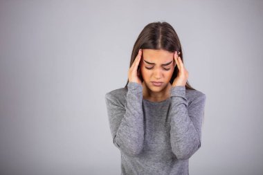 Başım ağrıyor. Umman el ele tutuşuyor ve gri arka planda dikilirken gözlerini kapalı tutuyor. Baş ağrısı çeken, strees hisseden bir kadın. Stüdyo fotoğrafı, günlük kıyafetler, gri arka plan..