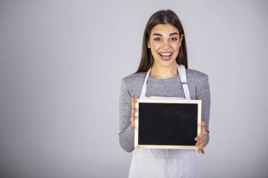 Üniformalı önlük giyen kadın işçi karatahta işareti taşıyor. Dost canlısı gülümseyen dükkan asistanı gri arka planda boş karatahta işareti tutuyor.. 