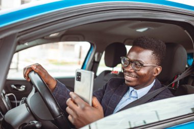 Araba sürerken bir adamın telefonunu kullanırken görüntüsü kesilmiş. İş mesajlaşması. Arabada cep telefonu kullanan bir iş adamı. Adam araba kullanırken cep telefonuna bakıyor.. 