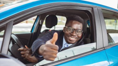 Yakışıklı, Afro-Amerikan traşsız, takım elbiseli, gözlüklü, direksiyonda el ele tutuşan ve baş parmağını kaldıran klas bir iş adamı. Mutlu adam portresi başparmak kaldırıyor