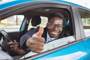 Yolculuk sırasında arabada otururken baş parmağını gösteren genç bir adamın portresi. Genç adam gülümsüyor ve baş parmağını kaldırıyor. Adam yeni arabasını seviyor..