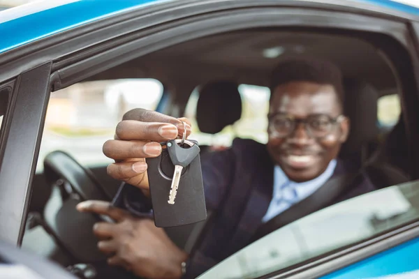 Portrait Of Young Happy Man Showing The Key Sitting In New Car. Young happy African American man sitting in a car and showing his car key while looking at camera.
