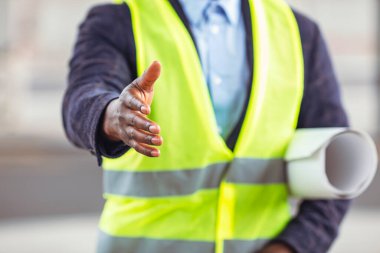 Koruyucu miğfer ve yelek giyen yakışıklı inşaat işçisi elini sıkmak için uzatıyor. El sıkışmaya hazır bir mimar - anlaşma, ortaklık ve kazan-kazan durumu konsepti